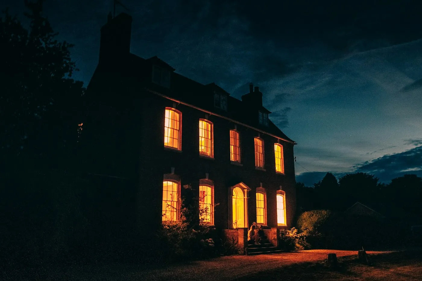 A stone house at night with every window lit amber