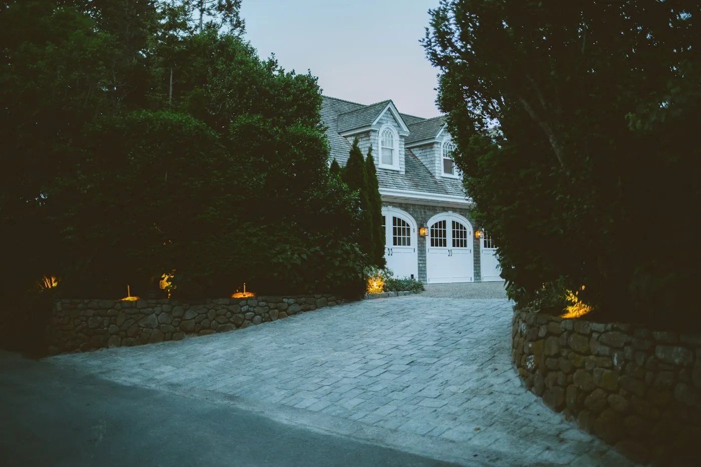 A shingled house at the end of a stone driveway surrounded by trees